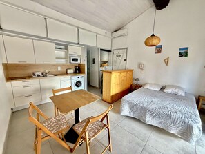 Une chambre compacte comprenant un lit, une petite table et une chaise. À côté se trouve une kitchenette équipée d’un four à micro-ondes, d’un grille-pain et d’un lave-linge.