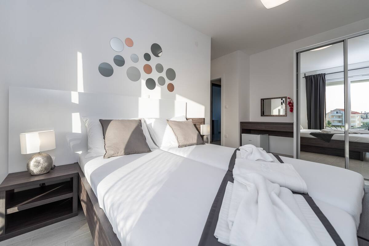 Une chambre d’hôtel moderne avec un grand lit, une table de chevet avec une lampe, un miroir et une vue sur l’extérieur grâce à une grande fenêtre.