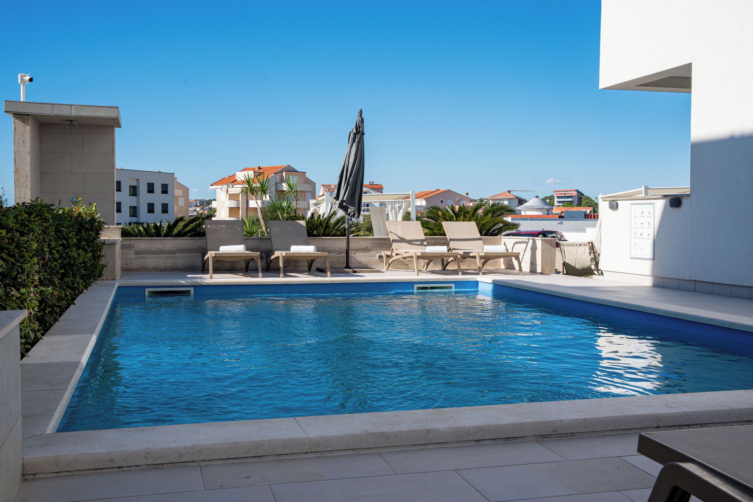 A swimming pool with lounge chairs and a pergola, surrounded by buildings.
