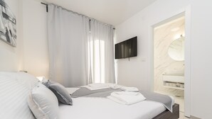 Une chambre moderne avec un lit, une télévision et une salle de bain dotée d’un lavabo en marbre et d’une douche.