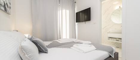 Un dormitorio moderno con cama, televisión, baño con lavamanos de mármol y ducha.