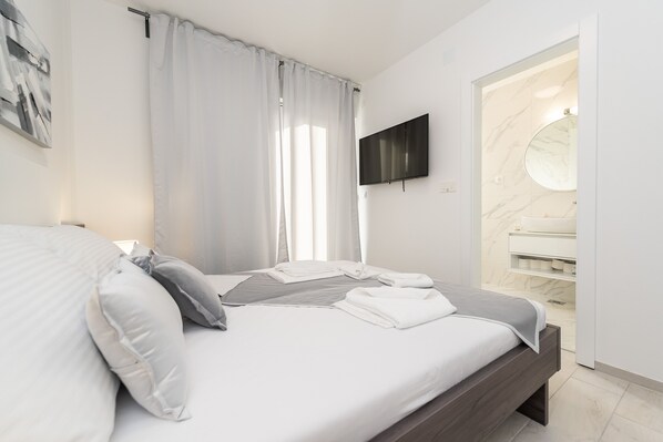 Un dormitorio moderno con cama, televisión, baño con lavamanos de mármol y ducha.