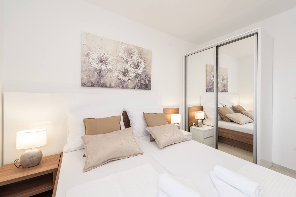 Une chambre d’hôtel moderne avec un grand lit, deux tables de chevet, une commode et un miroir.