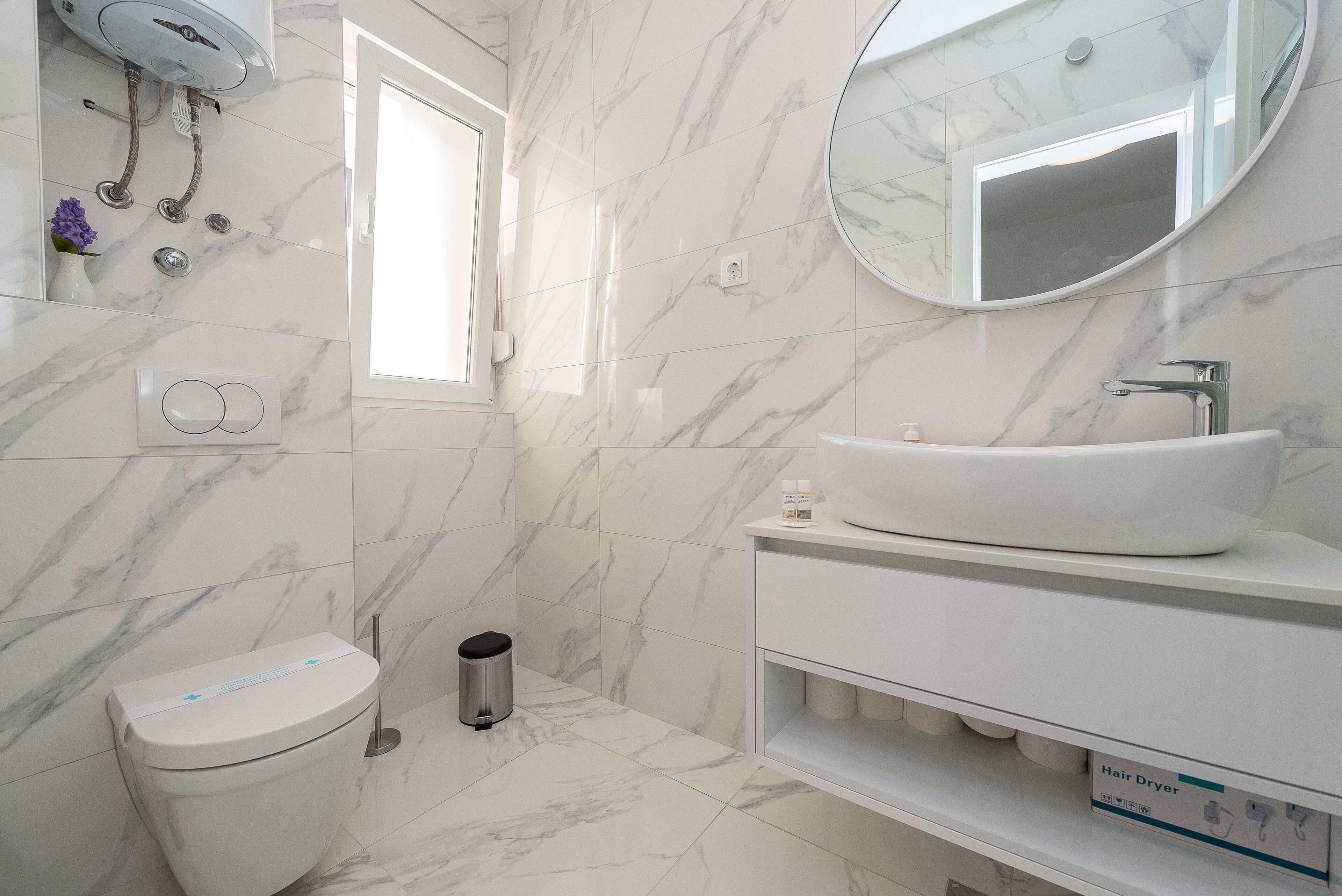 A modern bathroom with a white toilet, a sink with a mirror above it, and a window providing natural light.