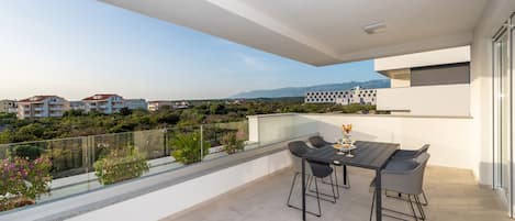 A balcony with a table and chairs, overlooking a cityscape with buildings and greenery.