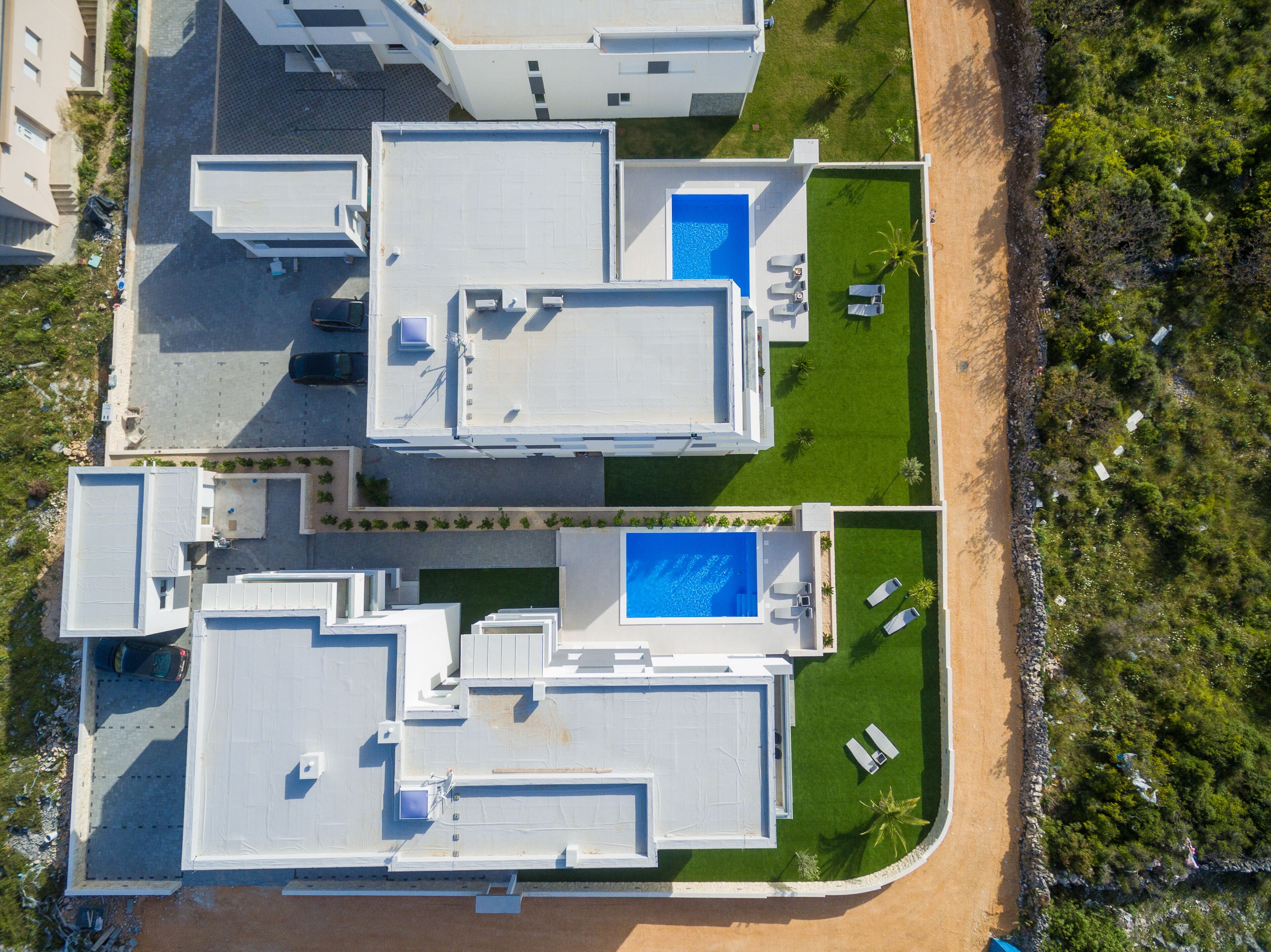 An aerial view of a modern hotel with multiple buildings, a central swimming pool, and a beach area.