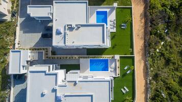 An aerial view of a modern hotel with multiple buildings, a central swimming pool, and a beach area.