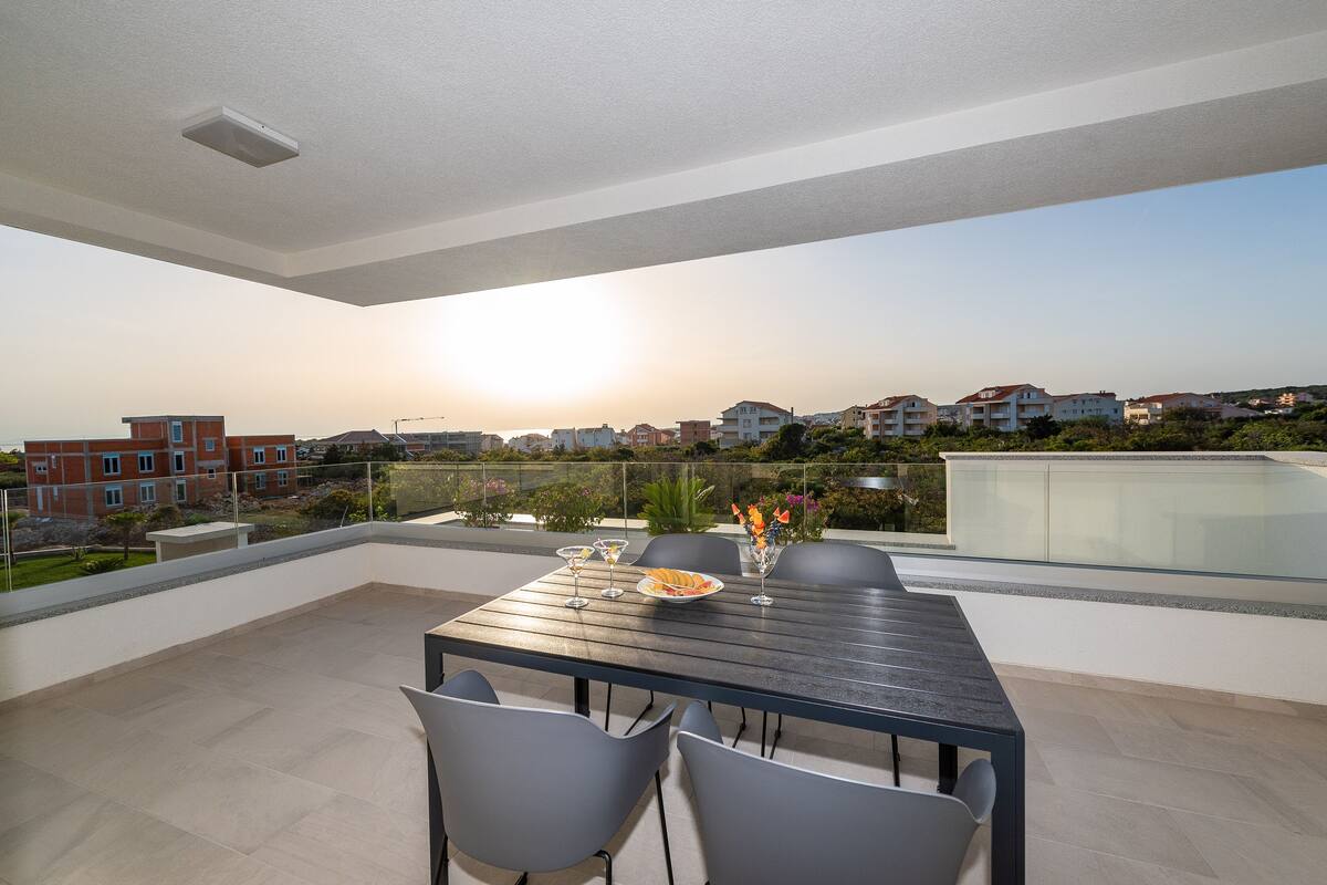 Un espace de restauration extérieur moderne, avec une table et des chaises, offrant une vue sur un quartier résidentiel au coucher du soleil.