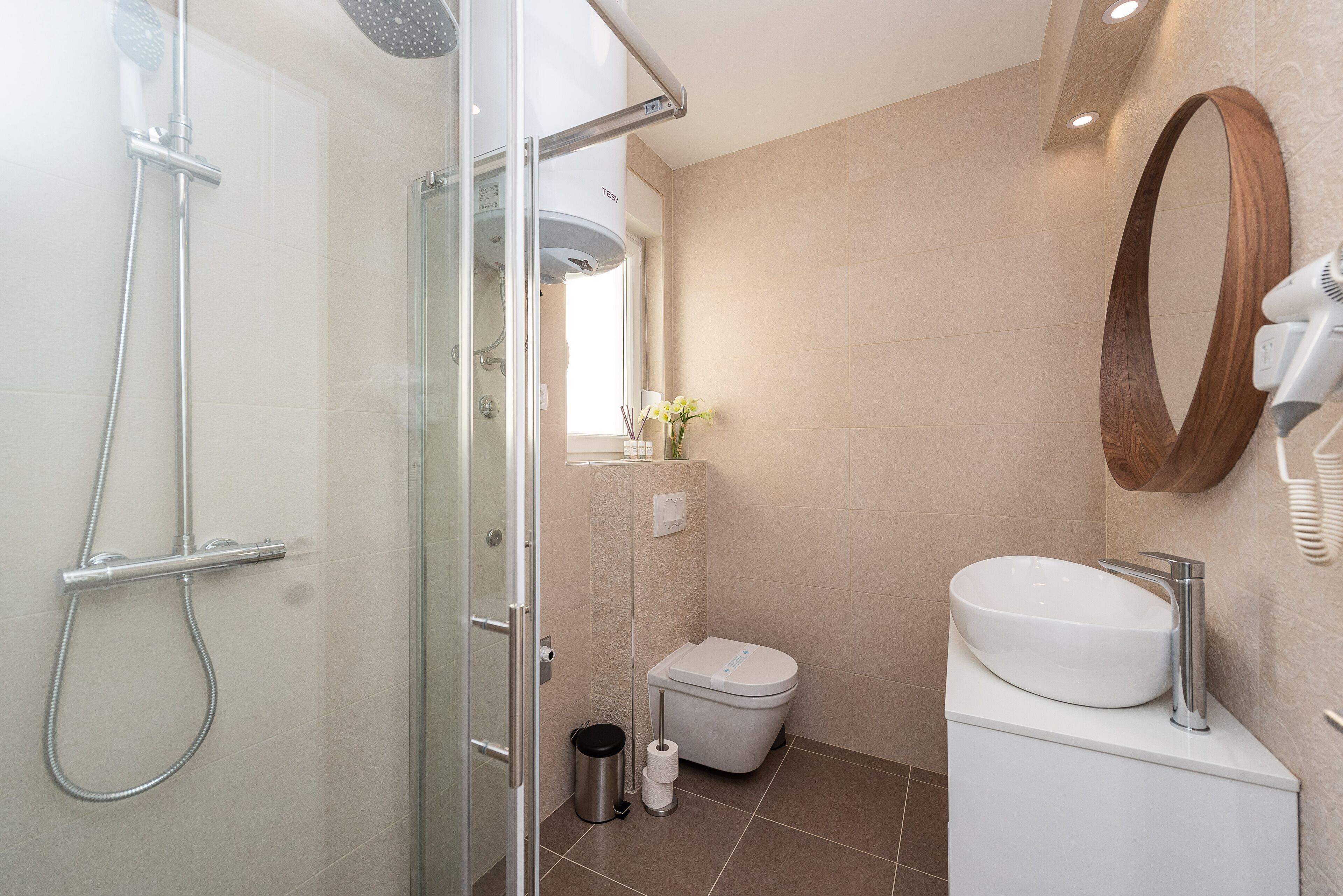 A modern bathroom with a glass shower enclosure, a white sink, and a wooden-framed mirror.