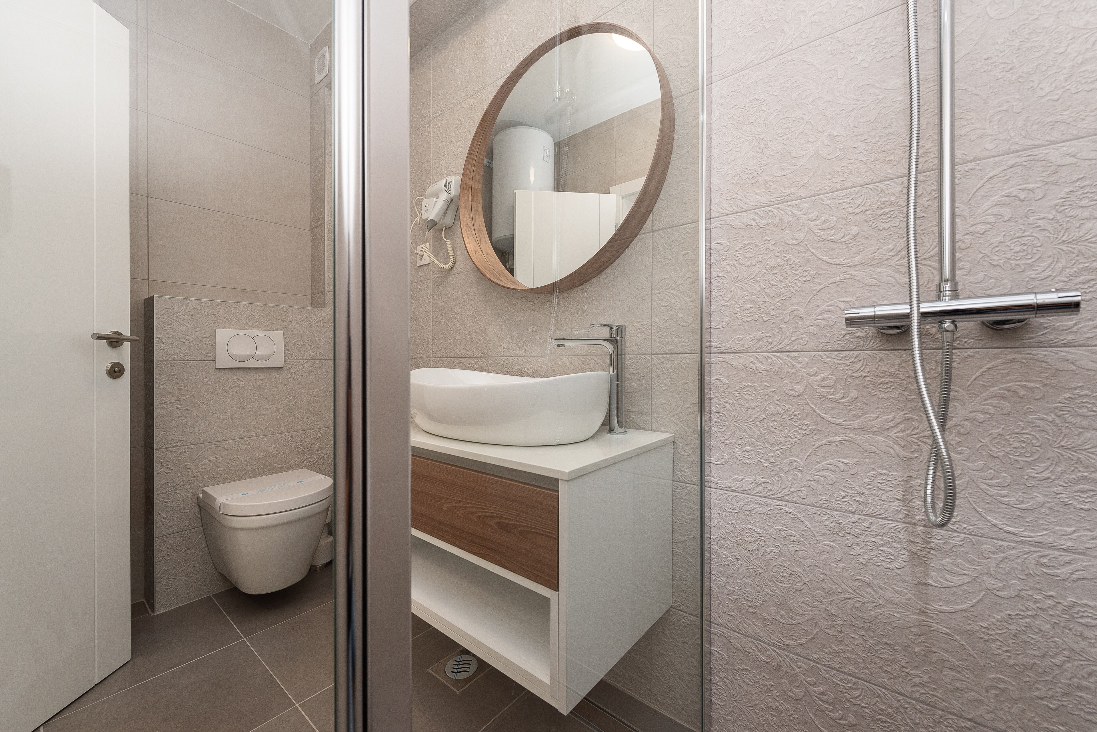 A modern bathroom with a glass-enclosed shower, a white sink with a wooden cabinet, and a toilet.