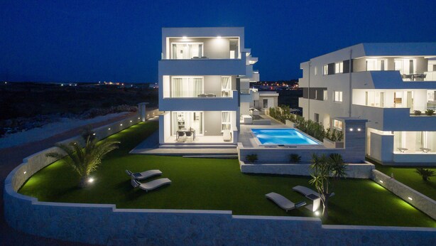 Un immeuble moderne à plusieurs étages, doté d’une piscine, d’un espace extérieur aménagé et d’une façade bien éclairée.