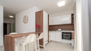 Une cuisine moderne avec des armoires blanches, un plan de travail en bois et un four encastré. On y trouve deux tabourets de bar blancs et un vase avec des fleurs posé sur le plan de travail.