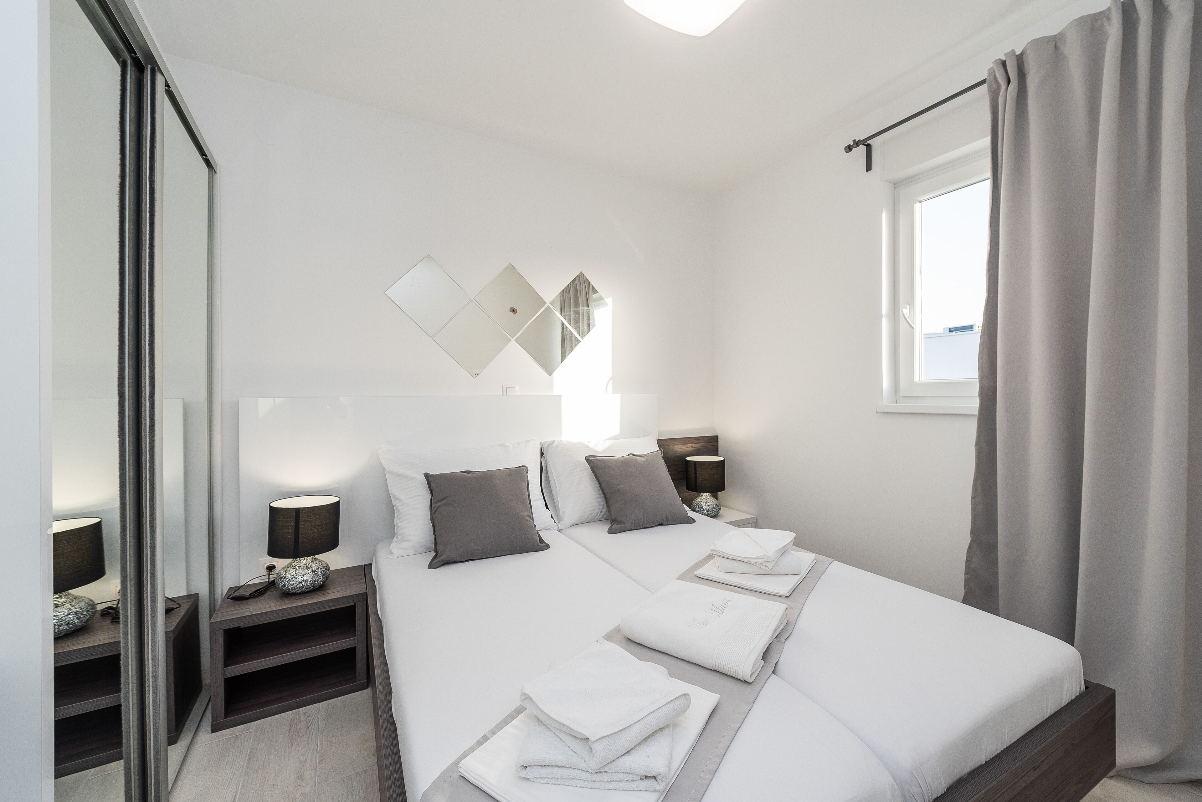Ein modernes Hotelzimmer mit einem großen Bett, Nachttischen, einem Spiegel und einem fenster mit Vorhängen.