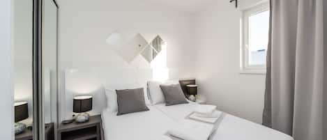 Ein modernes Hotelzimmer mit einem großen Bett, Nachttischen, einem Spiegel und einem fenster mit Vorhängen.