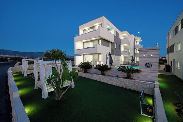 Un edificio moderno de varios pisos con zona de piscina, asientos exteriores y vista al mar.