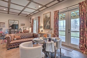Relax in this stylish living room with a leather sofa, armchair, and coffee table, surrounded by a large painting and a sliding glass door leading to a deck with outdoor views.