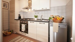 A modern kitchen with white cabinets, a stainless steel refrigerator, a stove, and a sink. - Appartamento Kennedy 1 (Diano Marina)