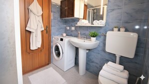 A modern bathroom with a wooden door, a washing machine, a sink, and a toilet. - Appartamento Kennedy 1 (Diano Marina)