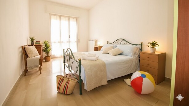 A bedroom with a bed, bedside table, lamp, chair, potted plants, and a beach ball. - Appartamento Kennedy 1 (Diano Marina)