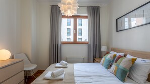 Ein Hotelzimmer mit Bett, Schreibtisch, Stuhl, einem Fenster mit Vorhängen und einem Wandbild.