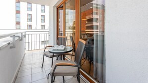 Ein Balkon mit Tisch und Stühlen, eine Glastür und Blick auf Gebäude.