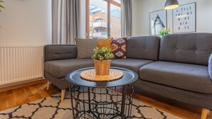 Ein modernes Wohnzimmer mit einem grauen Sofa, einem runden schwarzen Tisch mit einer gewebten Unterlage und einer schwarzen Uhr an der Wand.