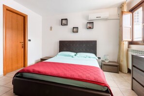 A bedroom with a bed, a wooden door, a nightstand, a bedside table, and a window with curtains.