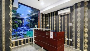 A reception area with a dark wood desk, patterned wallpaper, and a view of a parking lot through a large window. - Hotel Orchid (Lucknow)