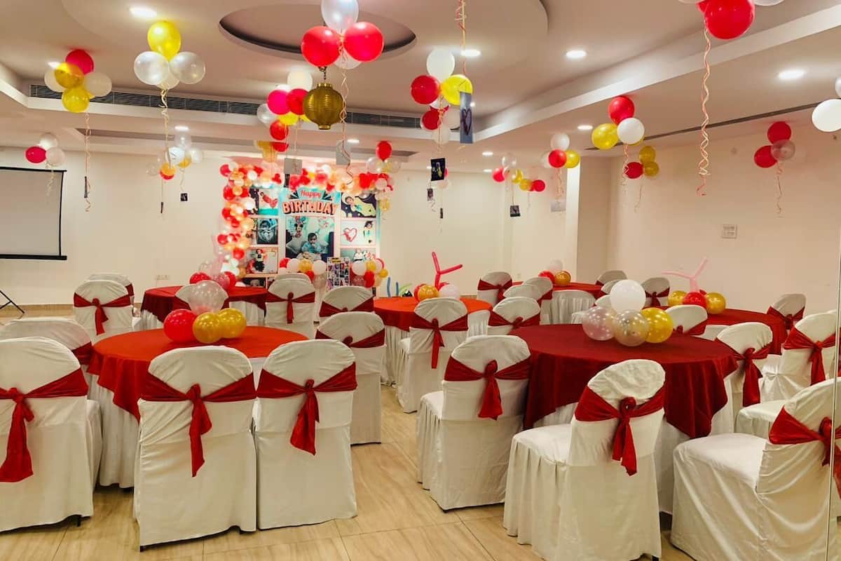 A conference room with round tables covered in red tablecloths, white chairs with red sashes, and balloons in red, white, and yellow.