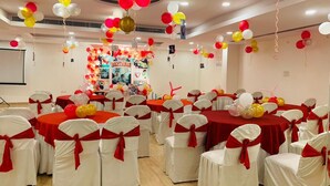 A conference room with round tables covered in red tablecloths, white chairs with red sashes, and balloons in red, white, and yellow. - Hotel Orchid (Lucknow)