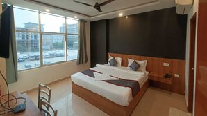 A hotel room with a large bed, a ceiling fan, a window with a view of buildings, and a desk with a chair. - Hotel Orchid (Lucknow)