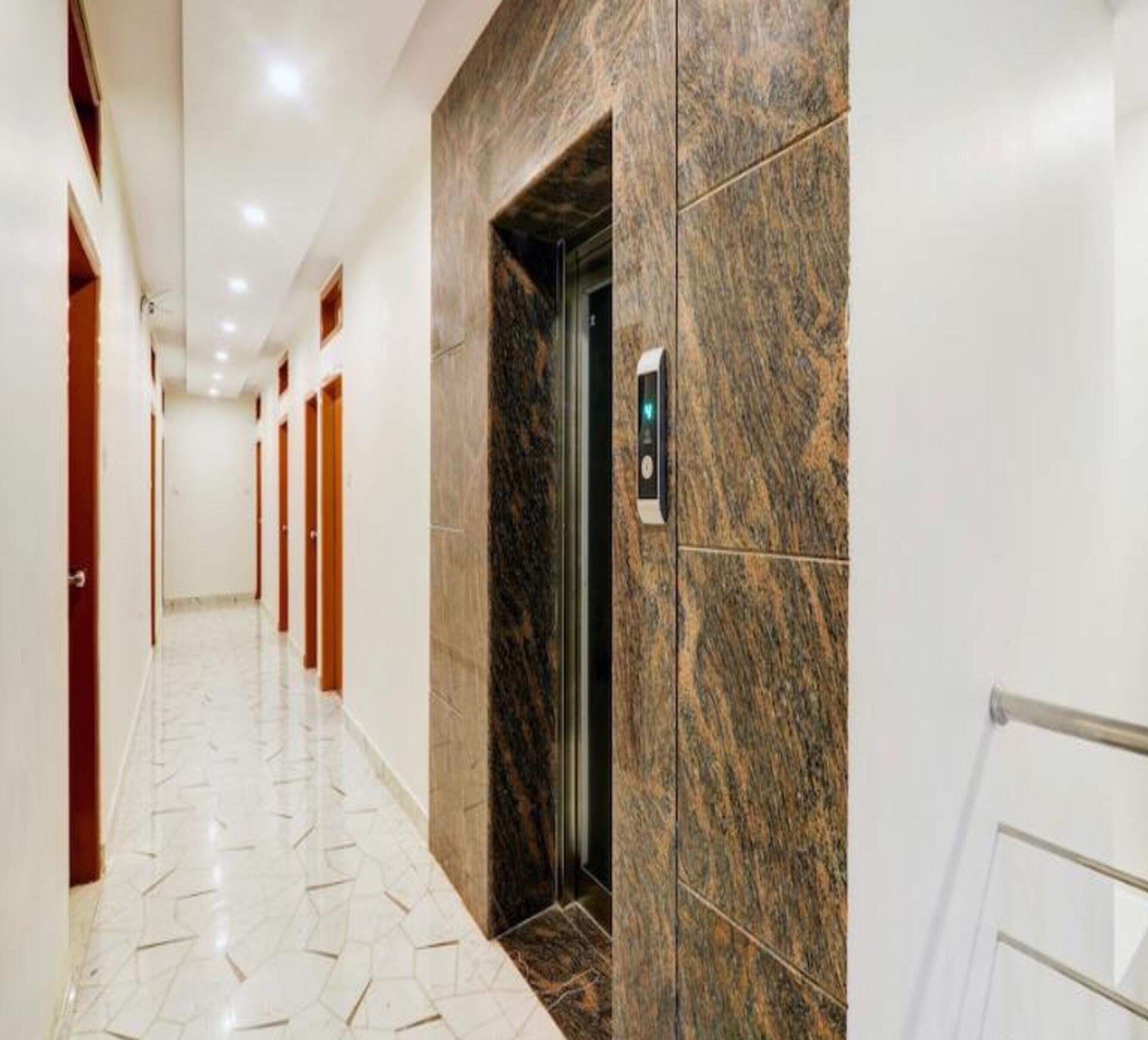 A hallway with a marble wall, an elevator, and a tiled floor.