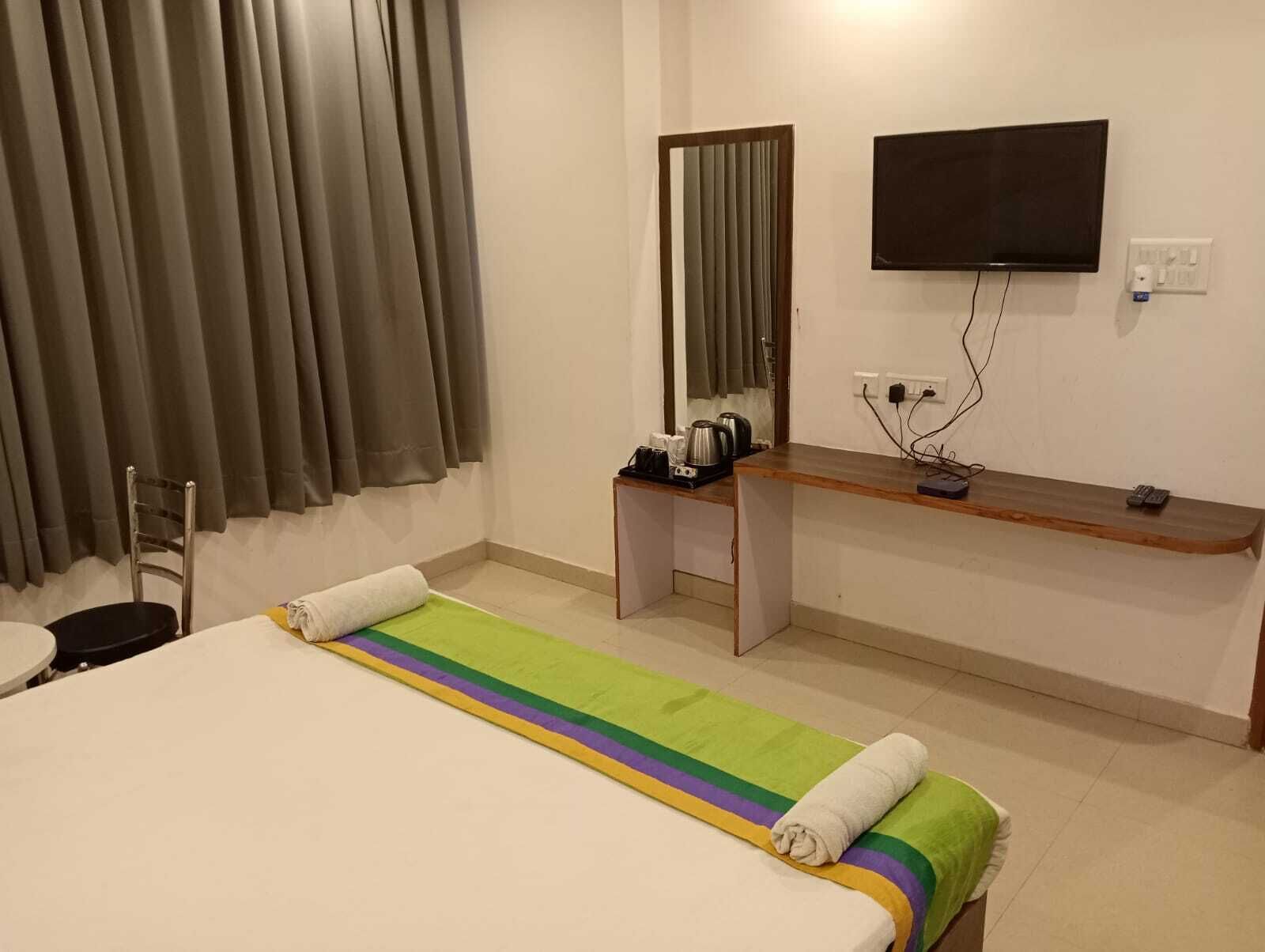 A hotel room with a bed, a desk, a chair, a television, and a window with curtains.