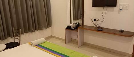 A hotel room with a bed, a desk, a chair, a television, and a window with curtains.
