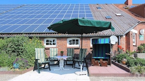 Een terras met een tafel, stoelen en een groene parasol.