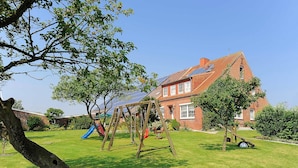 Een woonhuis met een bakstenen gevel, een schommel, een glijbaan en zonnepanelen op het dak.