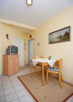 Uma pequena sala de jantar com uma mesa e cadeiras, uma televisão em um móvel e um quadro na parede.