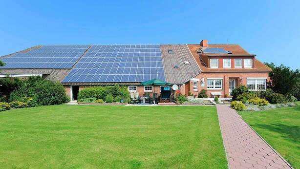 Een huis met een groot zonnepaneelveld op het dak en een gevel van baksteen.