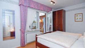 Een slaapkamer met een houten bed, een raam met gordijnen, een radiator en een kledingkast.