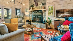 L’intérieur chaleureux d’un chalet avec une cheminée en pierre, des murs en bois et une grande fenêtre donnant sur une forêt.