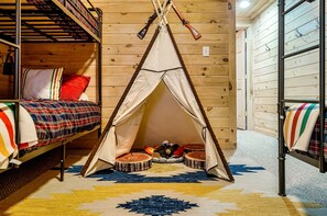 Una habitación acogedora con detalles de madera, una cama con ropa de cama escocesa, una tienda tipi y un pequeño hogar.
