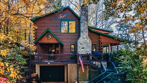 Une cabane en rondins avec une cheminée en pierre, une véranda et un escalier menant à une terrasse.