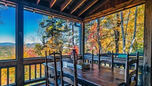 Une terrasse en bois avec une table et des chaises, donnant sur une forêt aux couleurs automnales.