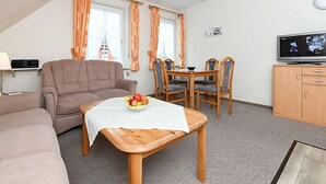 A cozy hotel room with a sofa, a dining table with chairs, a TV, and a small cabinet. - Vacation apartments in Huus Janssand in Bensersiel - Holiday apartment 1 (Esens)