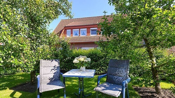 A garden with two chairs and a table, surrounded by lush greenery and a house in the background. - Vacation apartments in Huus Janssand in Bensersiel - Holiday apartment 1 (Esens)