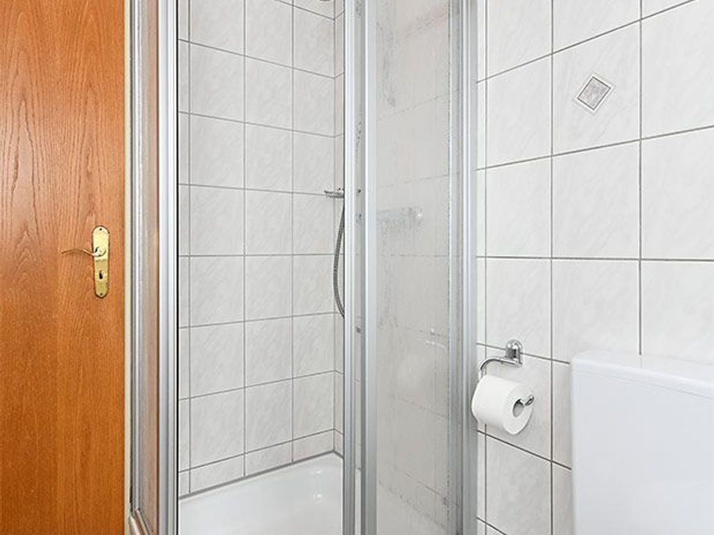 A bathroom with a shower, toilet, and a wooden door.