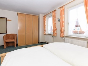 Camera d'albergo con due letti, un armadio, una sedia e una finestra con tende.