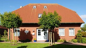 A two-story brick house with a red-tiled roof, a white front door, and two windows on the upper floor. - Vacation apartments in Huus Janssand in Bensersiel - Holiday apartment 1 (Esens)