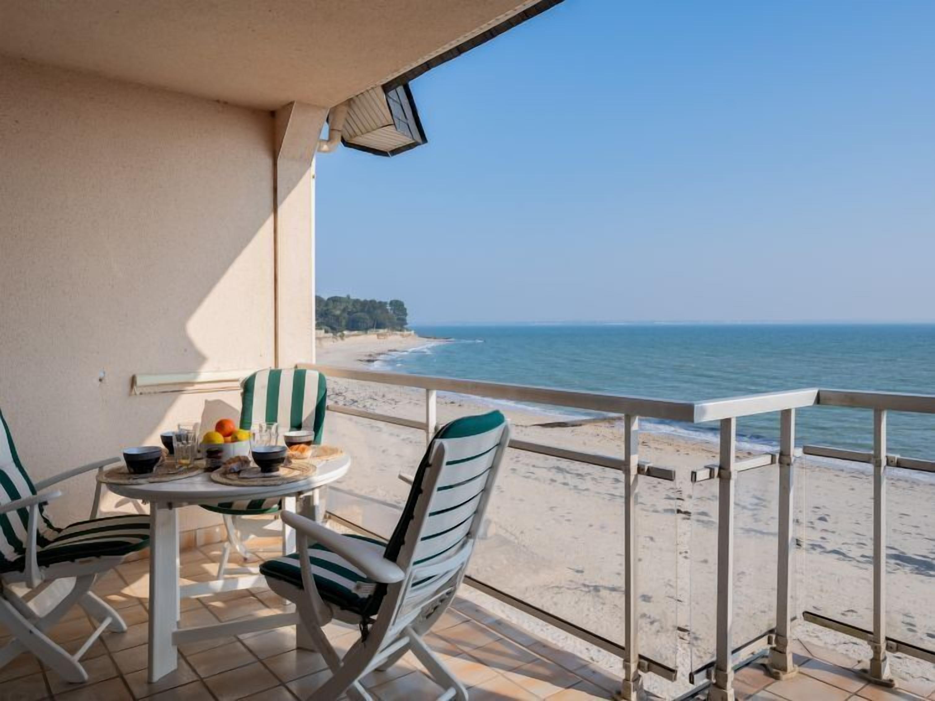 A balcony with a table and chairs, overlooking a beach.