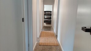 Un pasillo con piso de piedra pulida, un felpudo en la entrada y un banco negro a lo lejos.